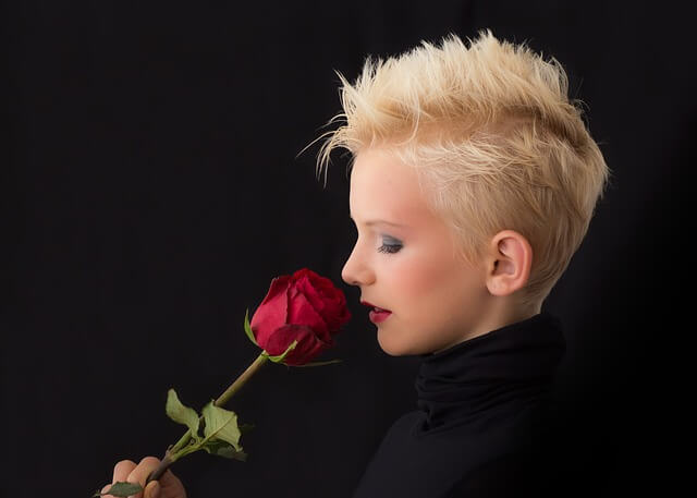 Blondwłosa kobieta wącha czerwoną różę