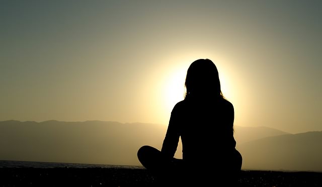 Siedząca na ziemi kobieta patrząca w stronę słońca